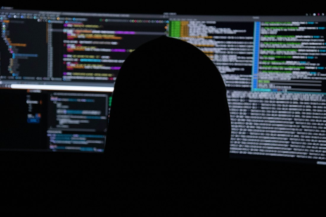 Analyst silhouetted in front of monitors showing code and logs